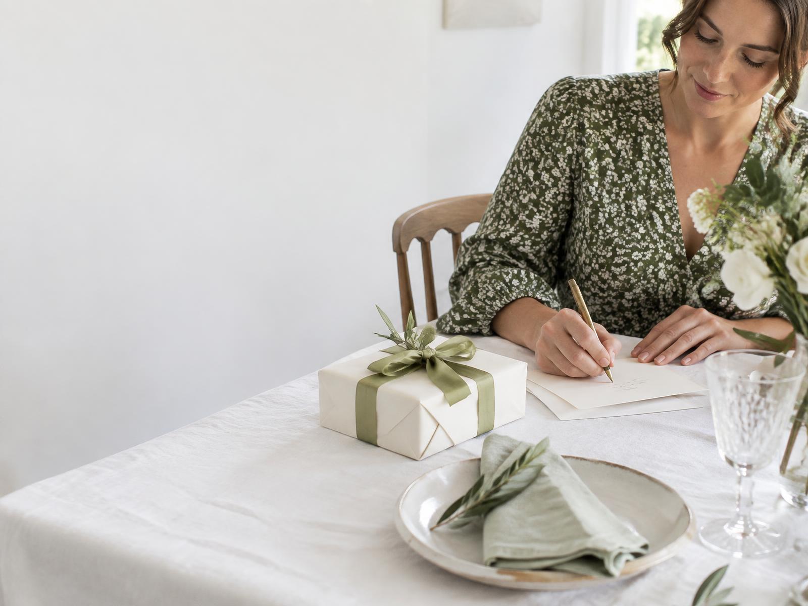 A wedding guest writing a personal card beside a simply wrapped gift at a set table